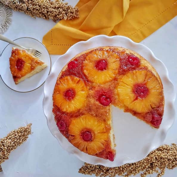 Pineapple Upside-Down cake on a cake stand, with a sliced up cake piece.