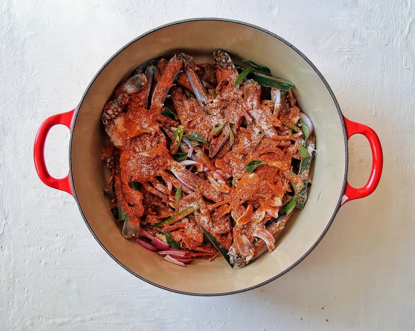 Red Le creuset pot with blue swimmer crab ready to be cooked into a curry. 